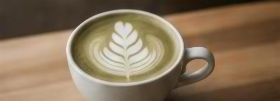 Matcha latte with leaf latte art in a ceramic cup on a wooden counter