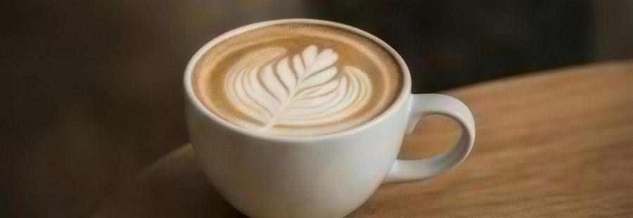 Cappuccino with fern latte art in a speckled ceramic cup on a wooden table