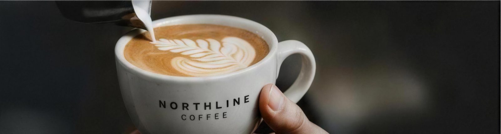 Steamed milk being poured into a Northline Coffee branded cappuccino, forming latte art